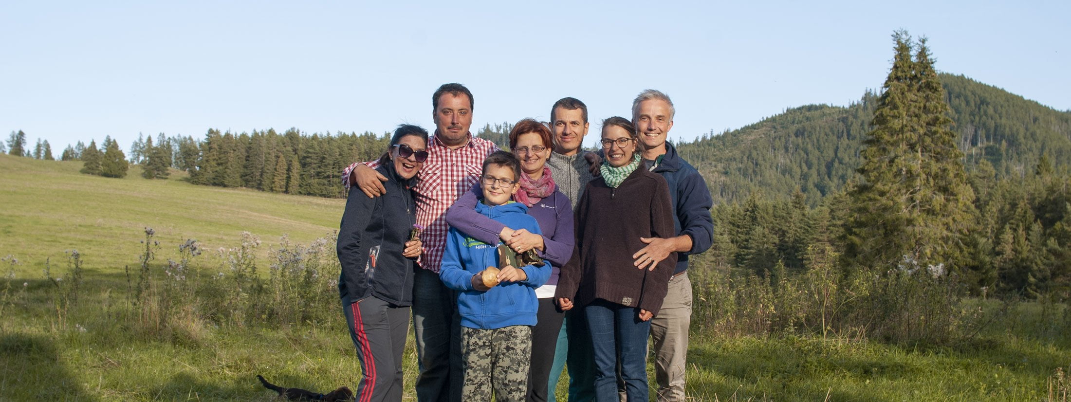 group of seven adult friends including a boy photographed on a meadow in pine woods