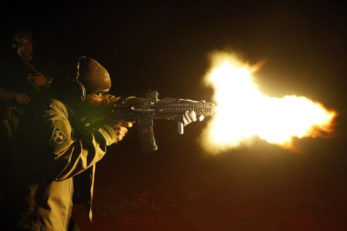 an angry man shooting from a firearm night time flames out of its barrel