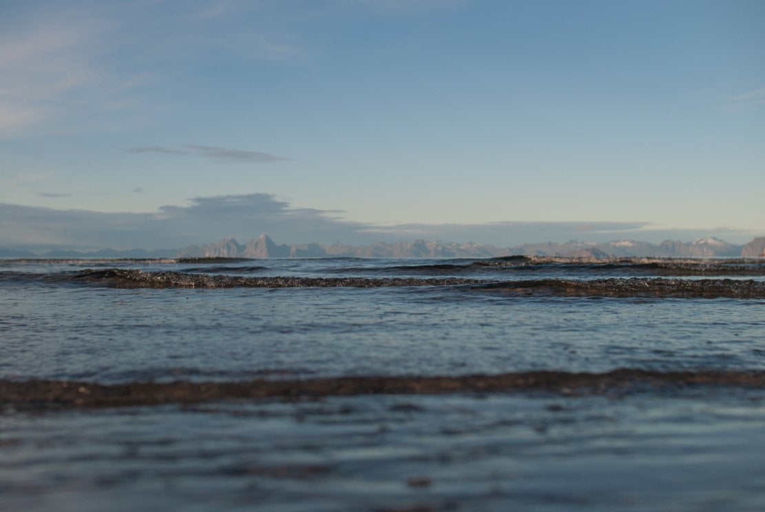 sea waves approaching during a bright day with low sun and mountains of Lofoten rising from the Norwegian sea