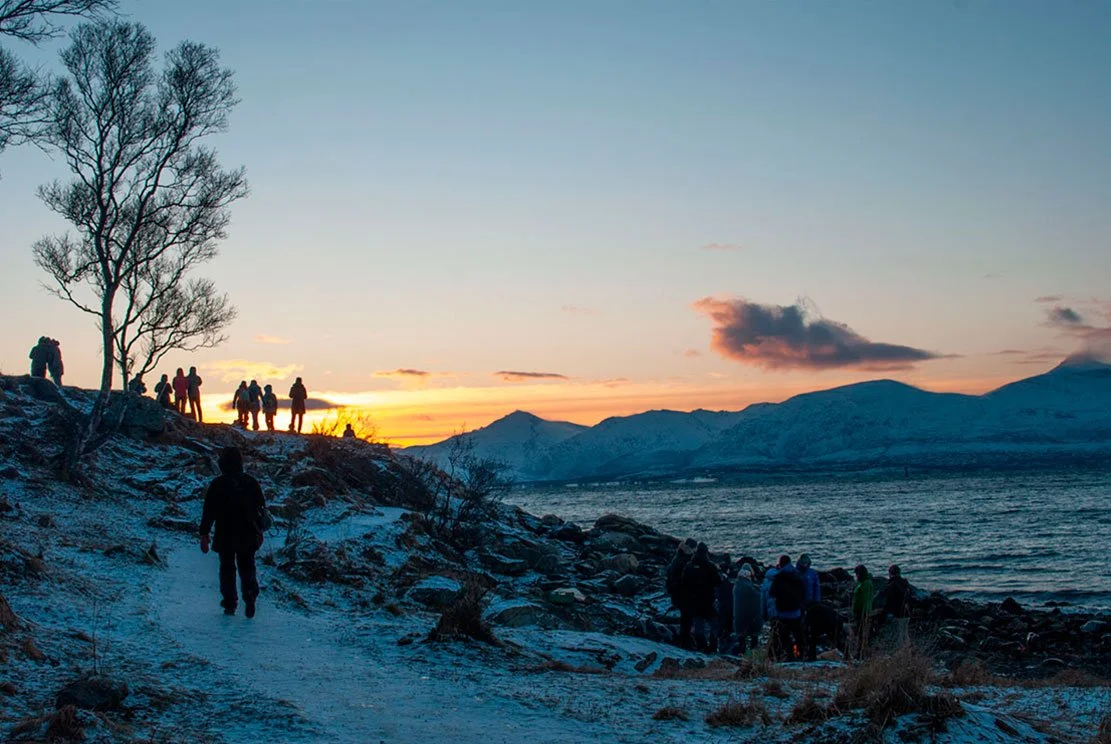 a winter beach and sea with mountains at the back and sun that came back after polar night in Tromsø hovering slightly at the horizon at midday 